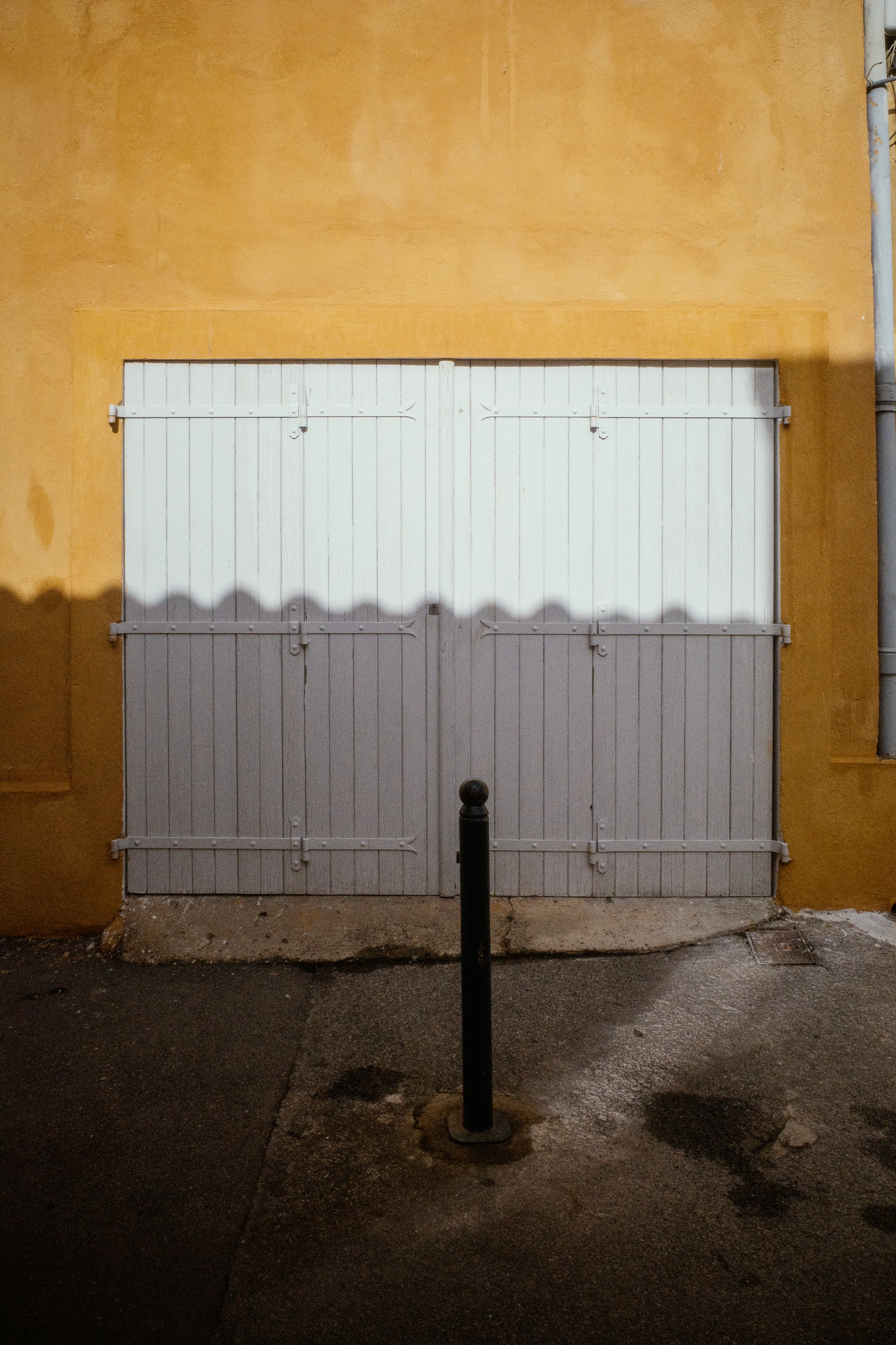 A white wooden door set in a yellow wall with a shadow and a black bollard in front.