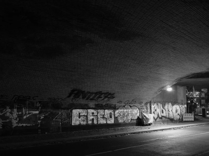 A graffiti-covered underpass with dim lighting and a covered object beneath.