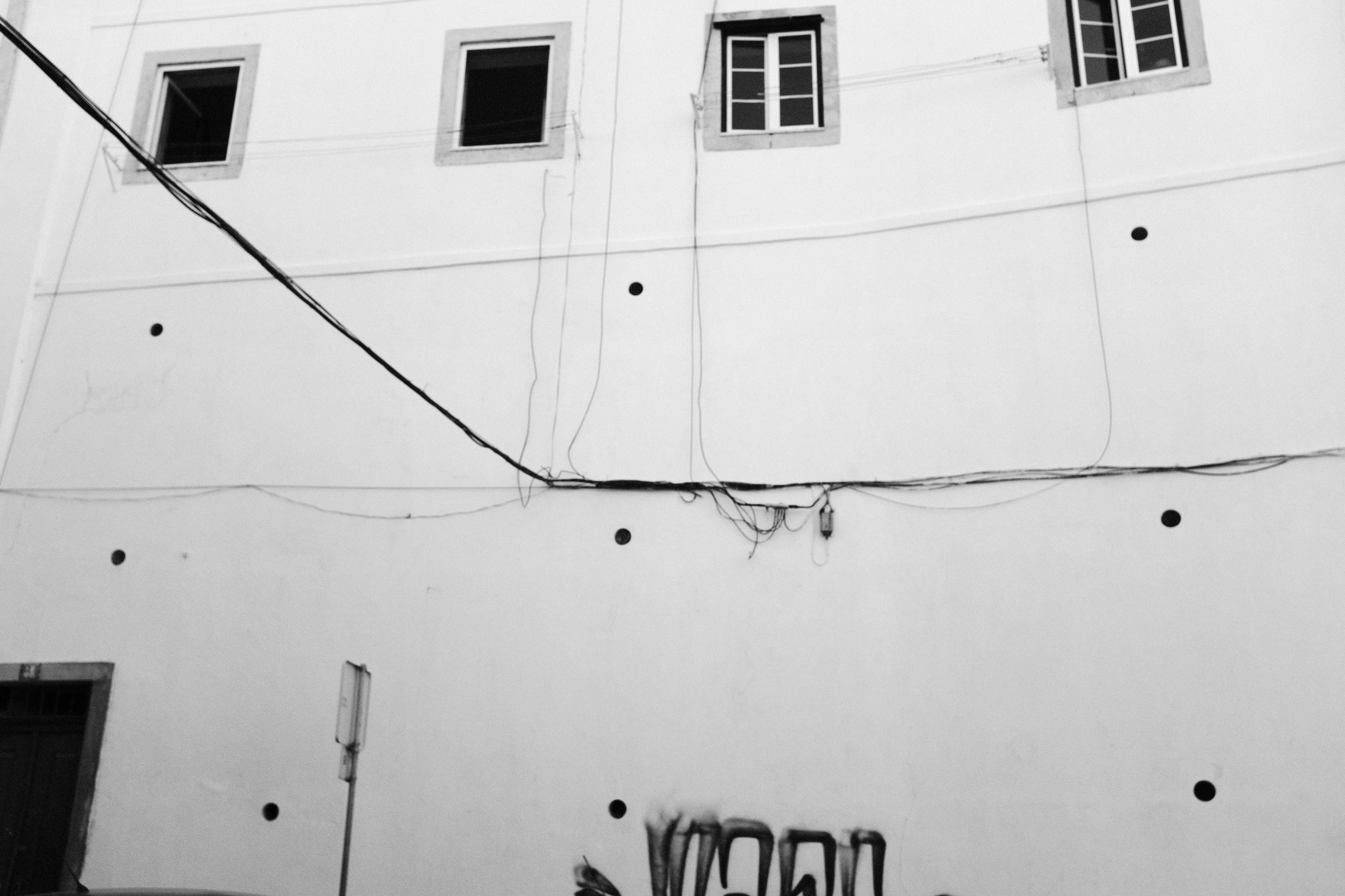 Black and white image of a building facade with three windows and visible wires.