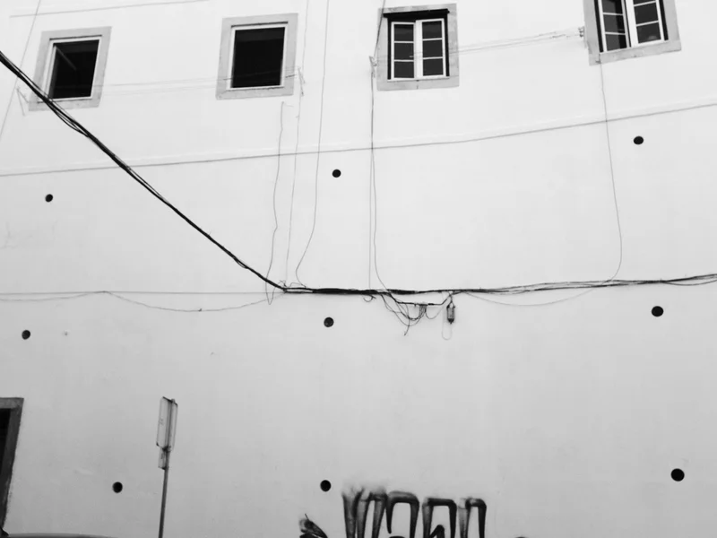 Black and white image of a building facade with three windows and visible wires.