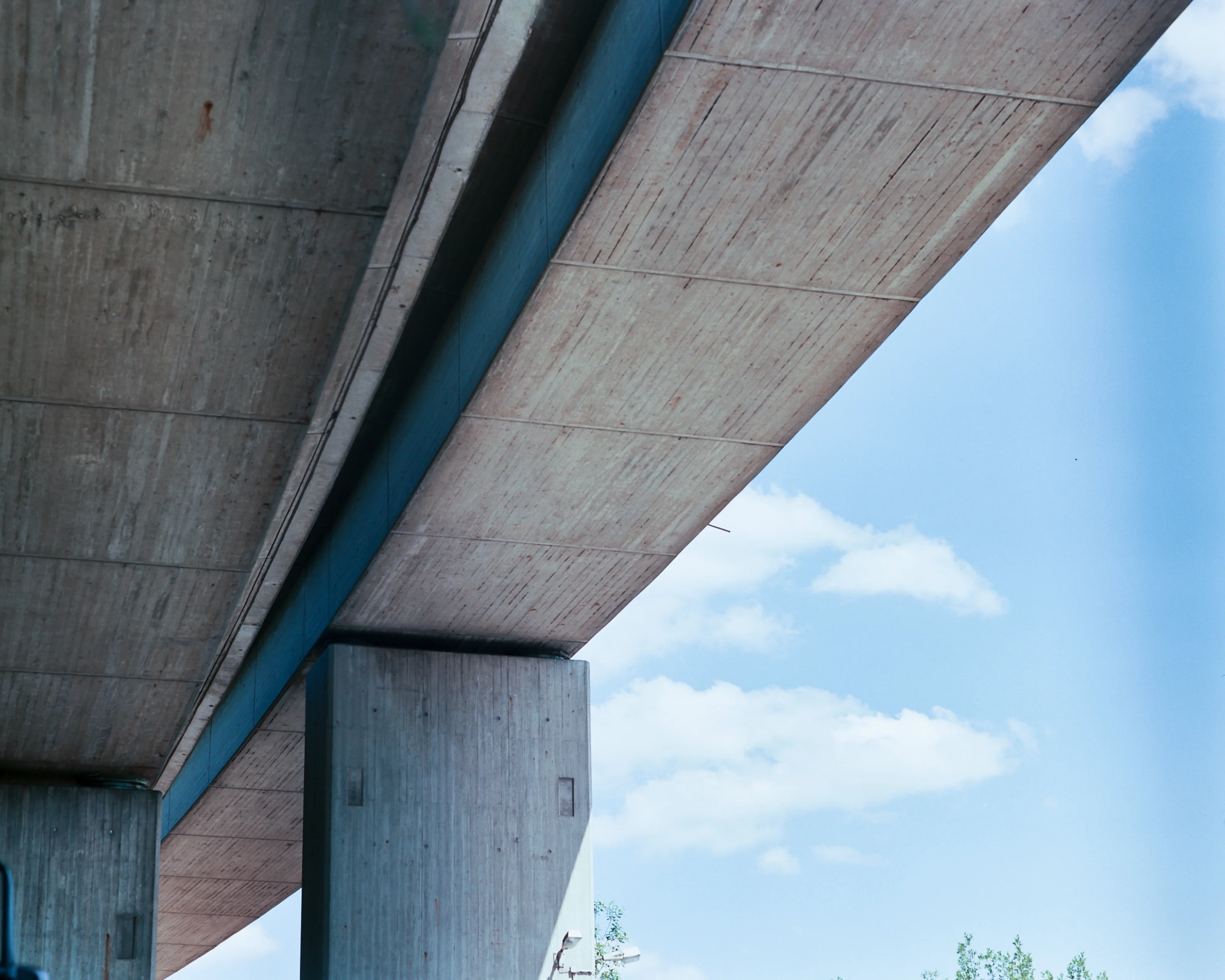 View of an overpass with concrete pillars against a blue sky with clouds.