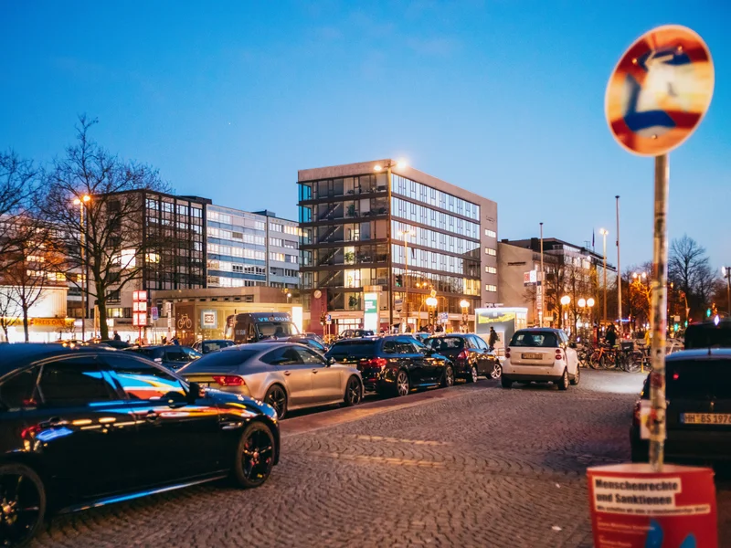 City street at dusk with parked cars and modern buildings in the background.