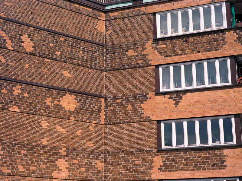 Brick building facade with large windows and irregular patterns.