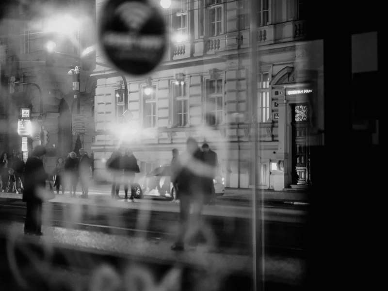 Blurry silhouette of people walking near a building at night.