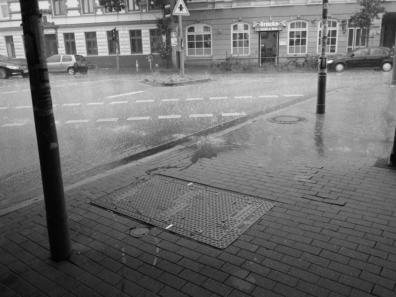 Street view of heavy rain pouring onto a city sidewalk and road intersection.