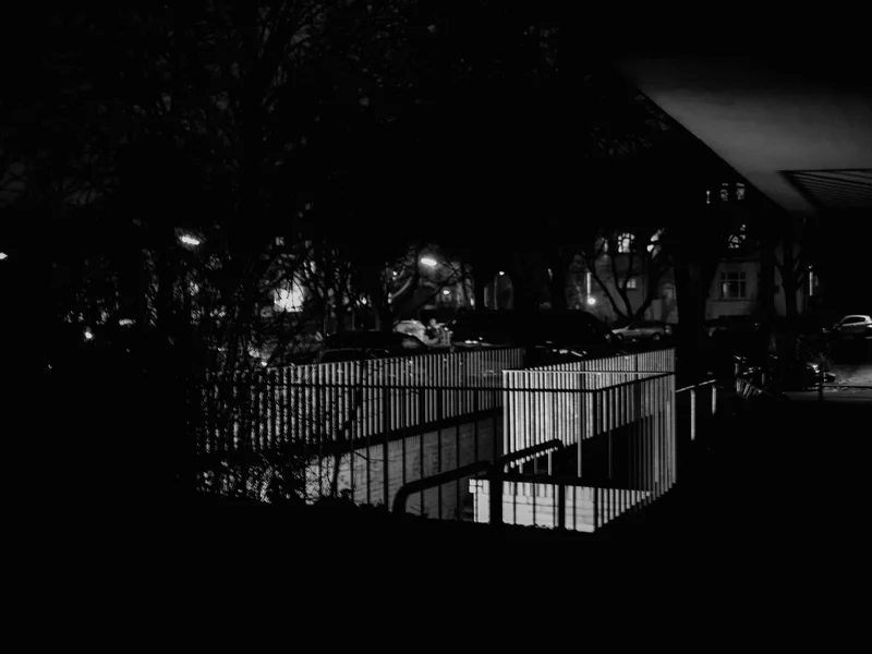 A nighttime scene showing illuminated railings and shadows in an urban environment.