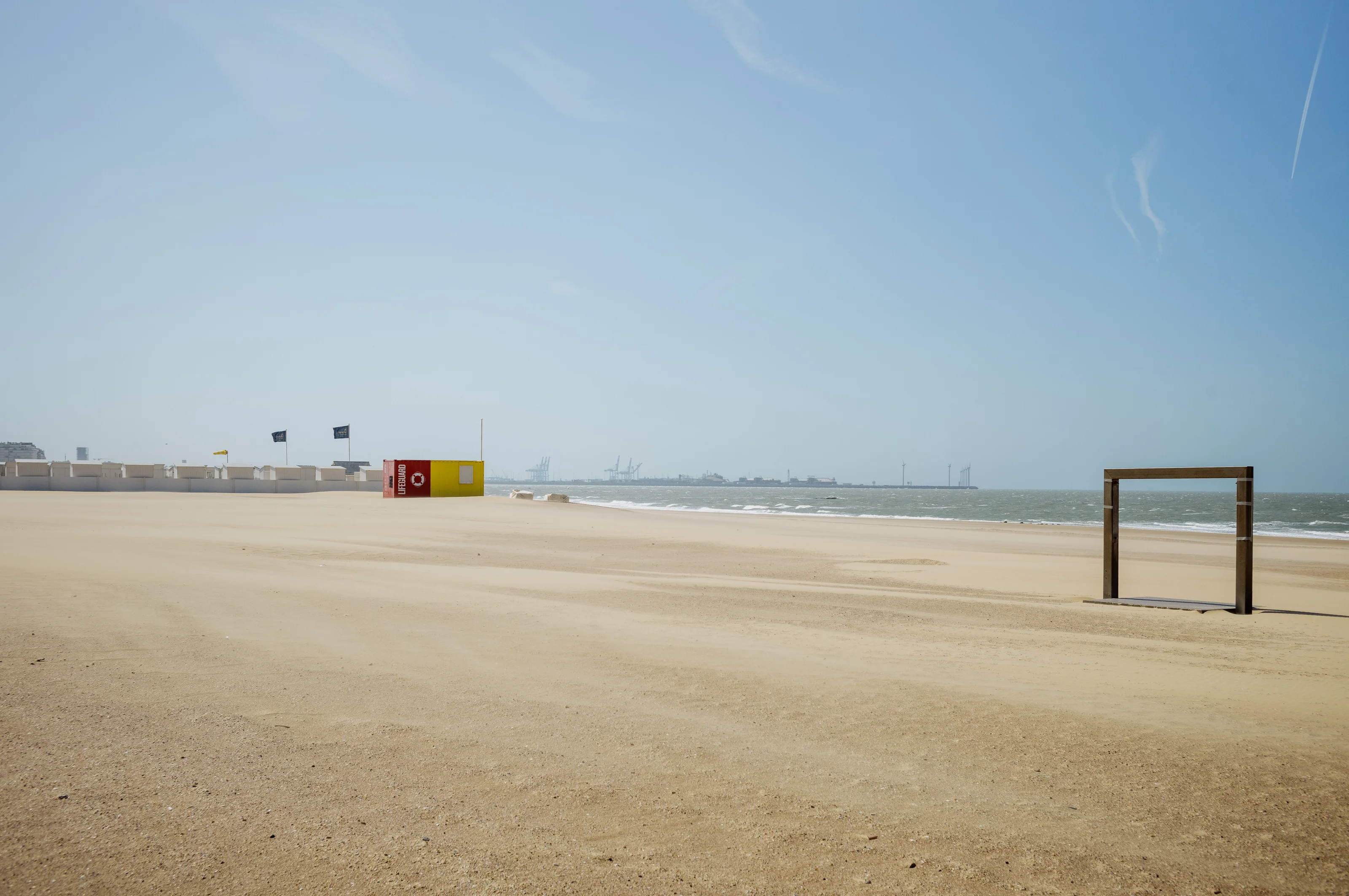 A sandy beach with a lifeguard station and a wooden frame overlooking the sea, under a clear blue sky.