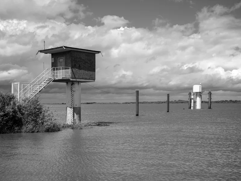A water monitoring station elevated on a platform above water with a cloudy sky.