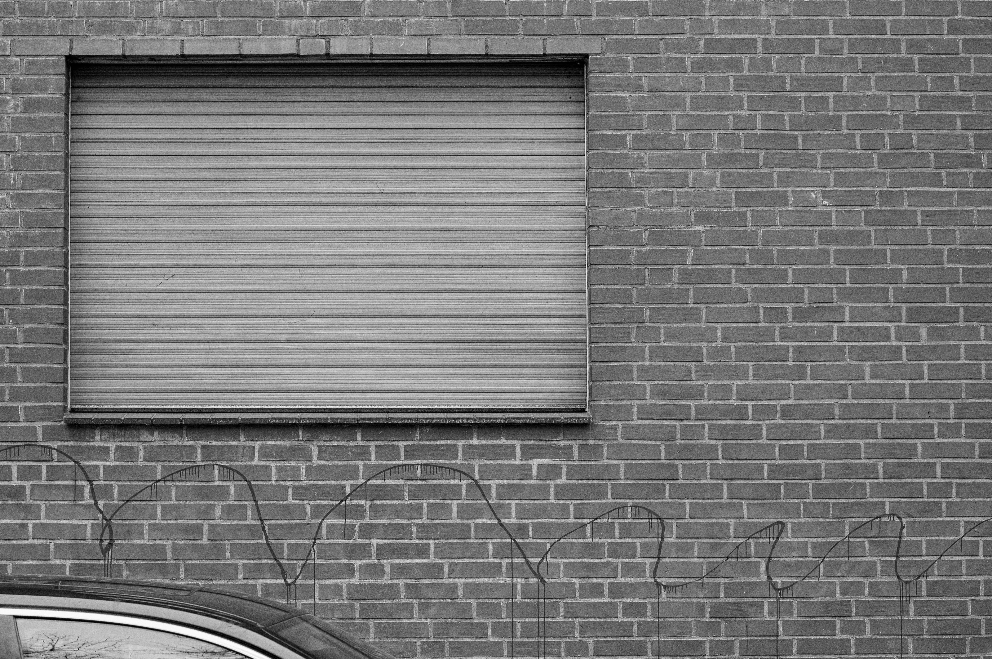 A closed roll-up shutter on a brick wall with the top of a car visible in the foreground.