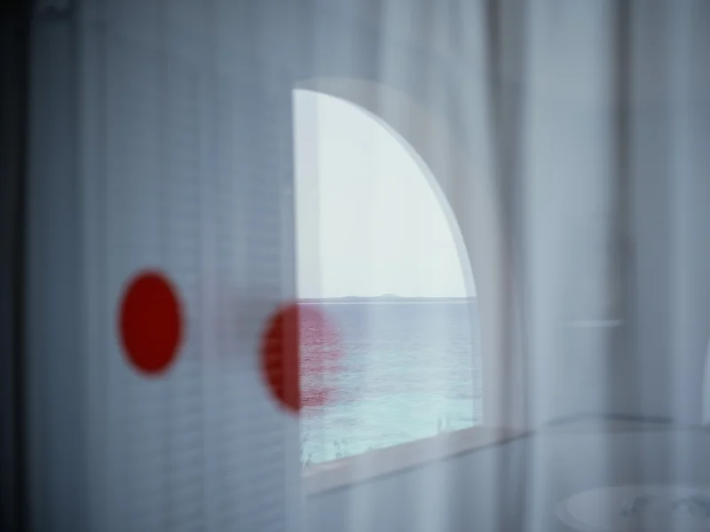 View through a window with reflections of red dots and a sea horizon visible outside.