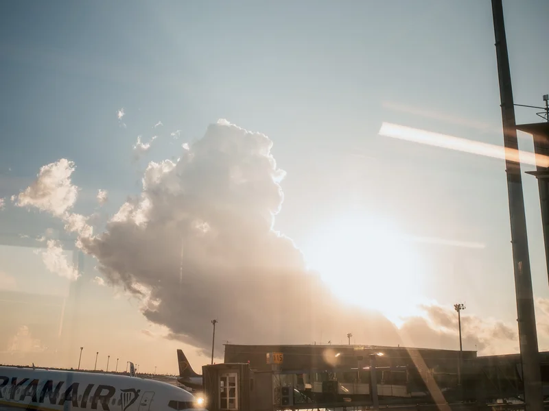 Airplane parked at an airport gate with a dramatic sunrise and clouds in the background.