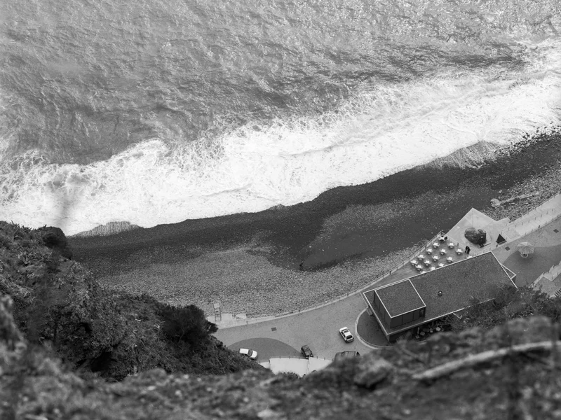 Aerial view of a coastline with waves, a pebble beach, and a nearby building.