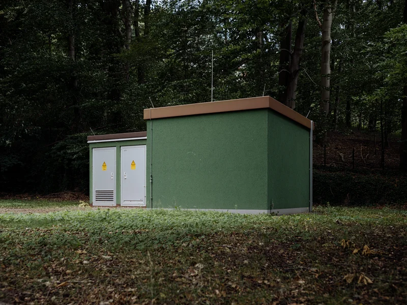 A small green electrical utility building in a forested area.