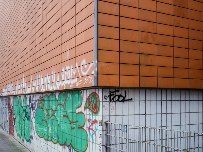 A building corner with orange tiles and graffiti on its lower walls.