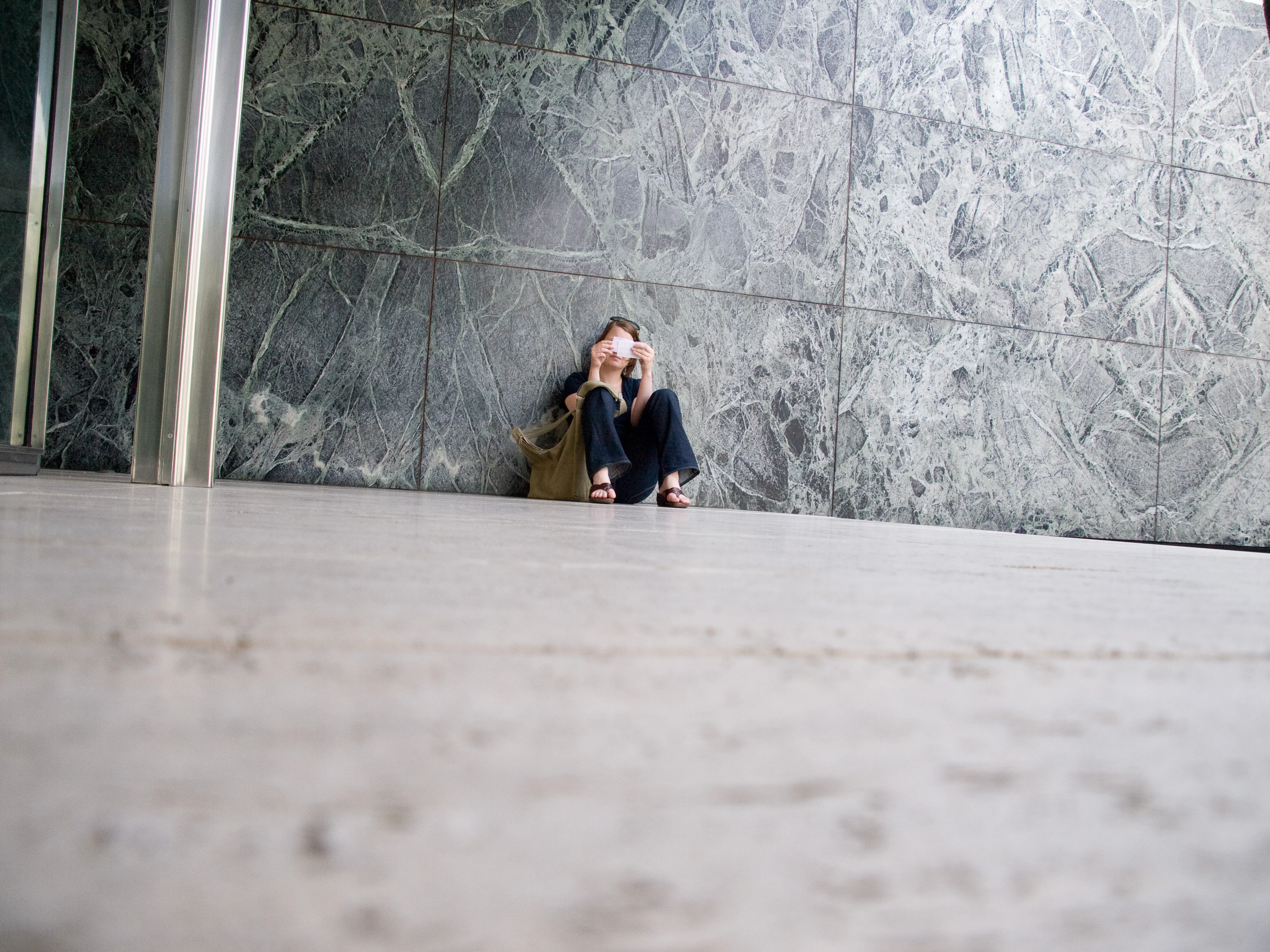 Person sitting against a marble wall, reading a book.