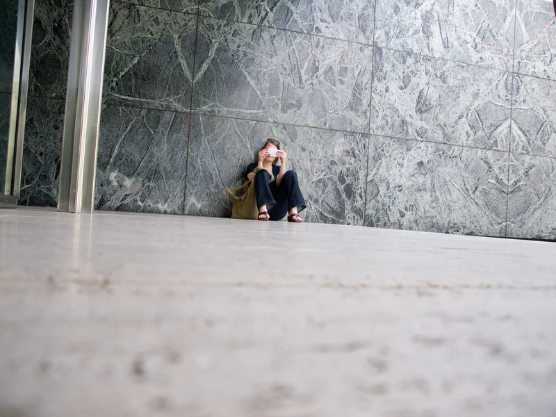 Person sitting against a marble wall, reading a book.