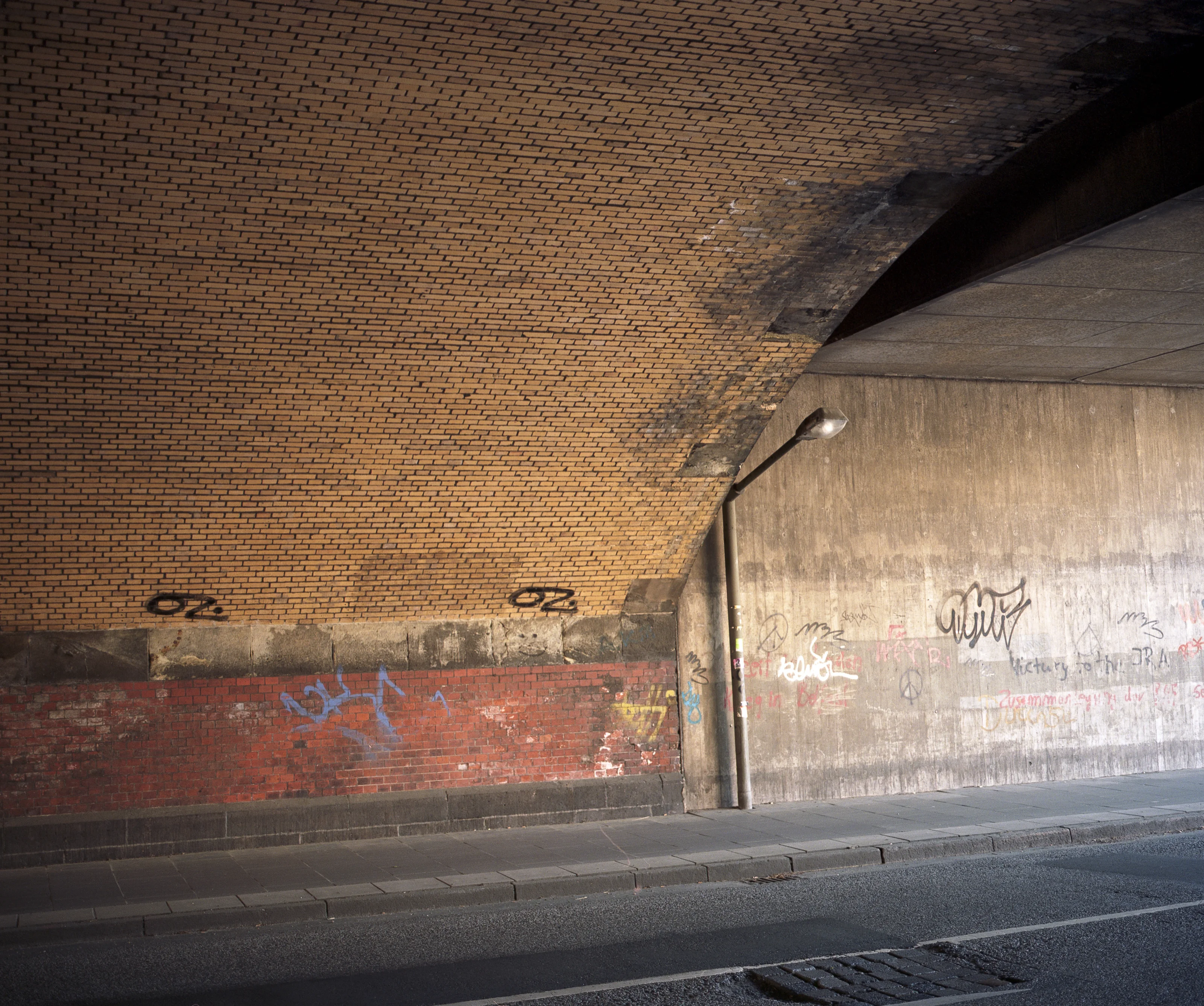 Underpass with brick and concrete walls covered in graffiti, illuminated by sunlight.