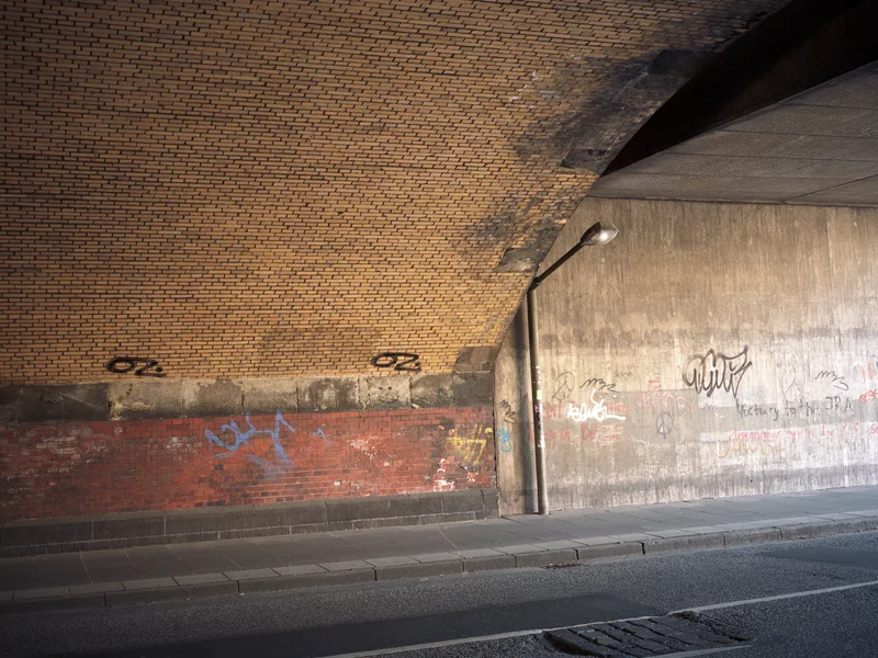 Underpass with brick and concrete walls covered in graffiti, illuminated by sunlight.