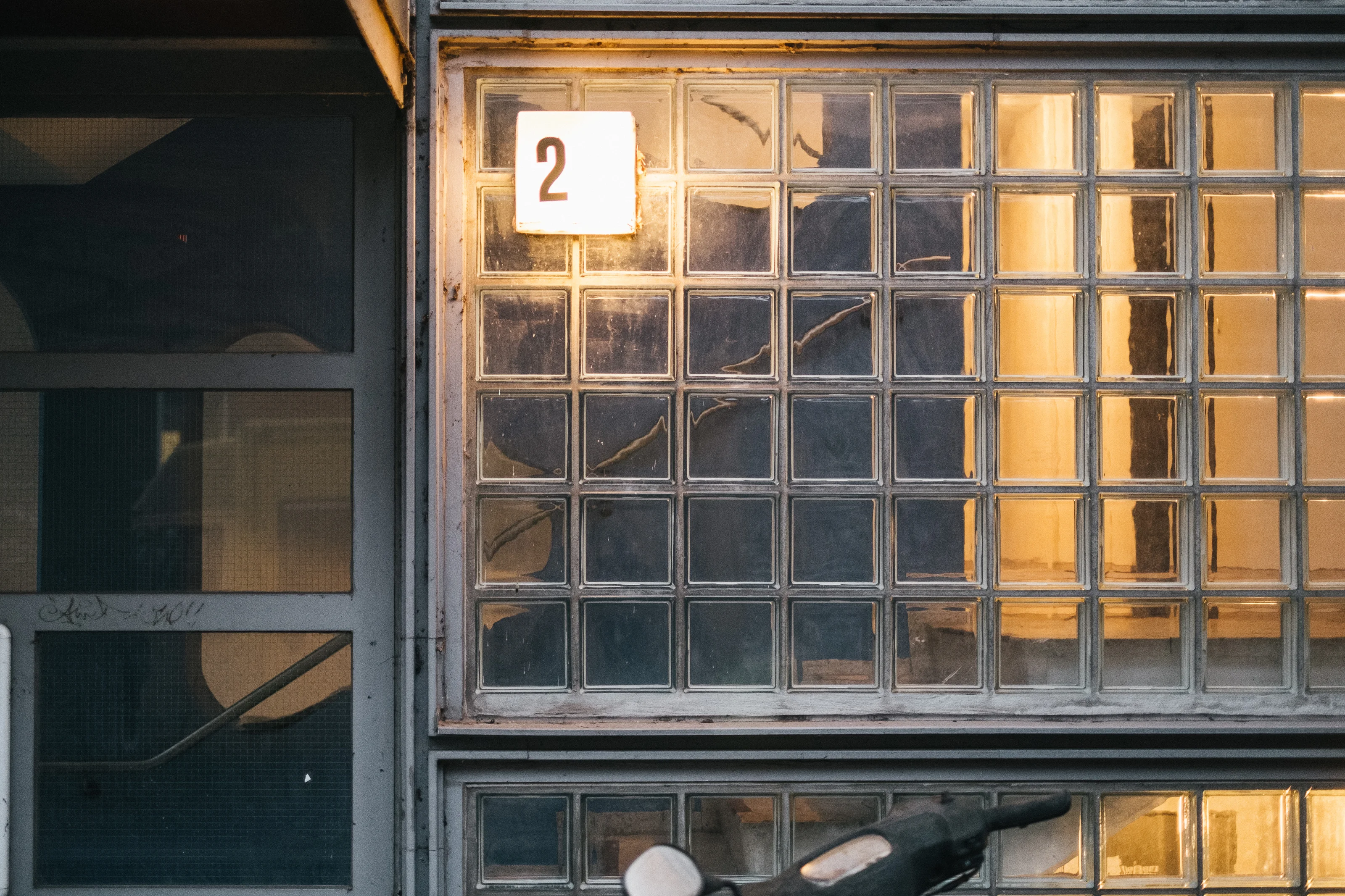 A numbered window with a sign '2' above a grid of textured glass blocks.
