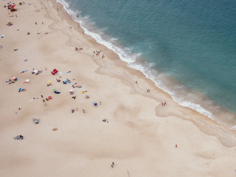 Aerial view of a busy beach with people, umbrellas, and waves meeting the shore.