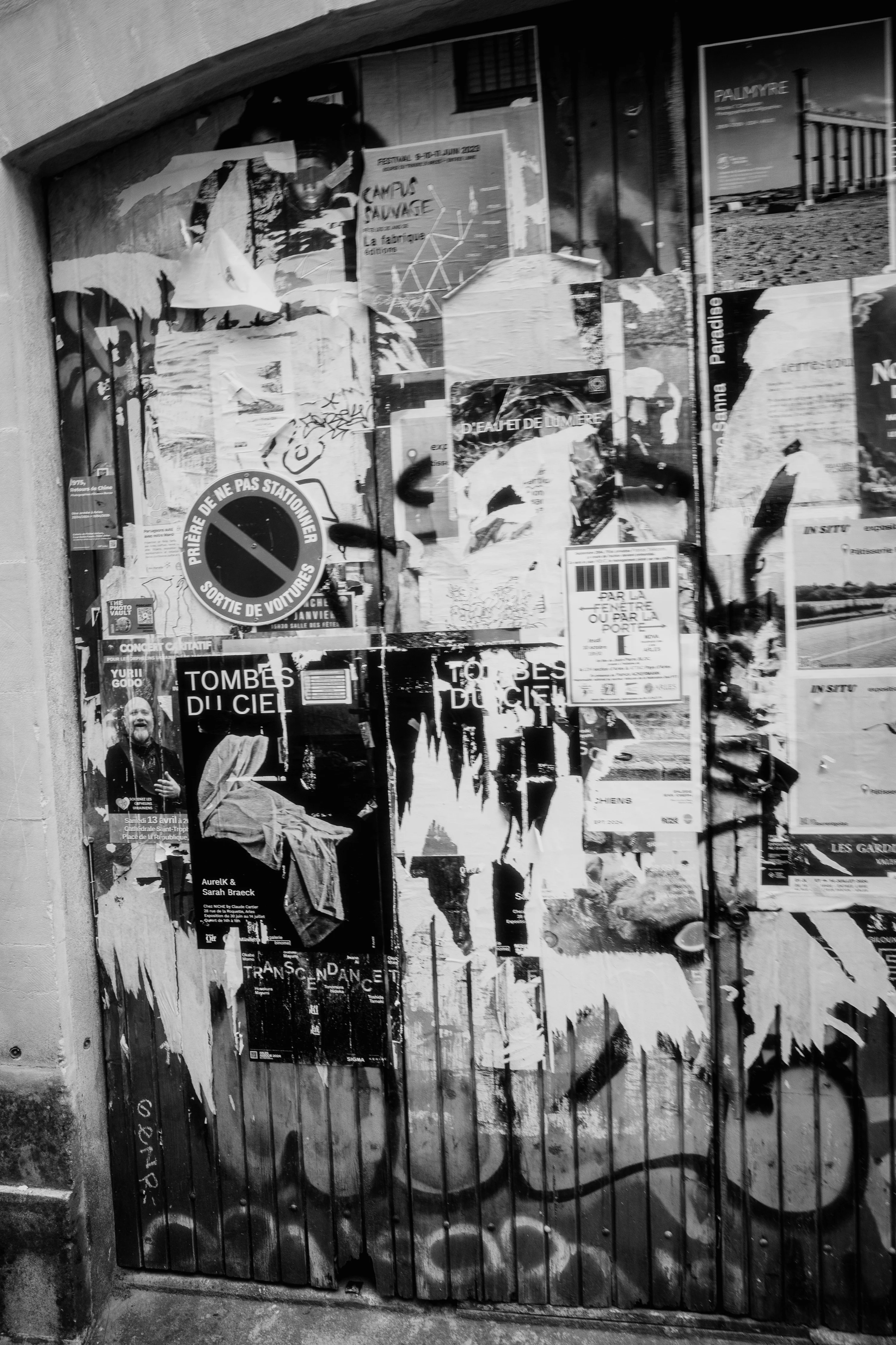 Black and white photo of a wooden door covered with various torn posters and graffiti.