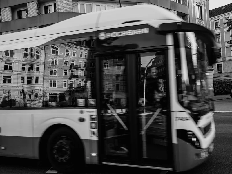 A black and white photo of a bus in motion with a reflection of a building on its windows.