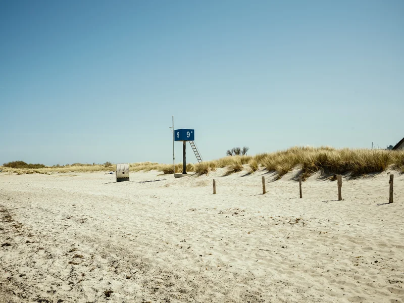 A sandy beach with a blue lifeguard station and grassy dunes in the background.