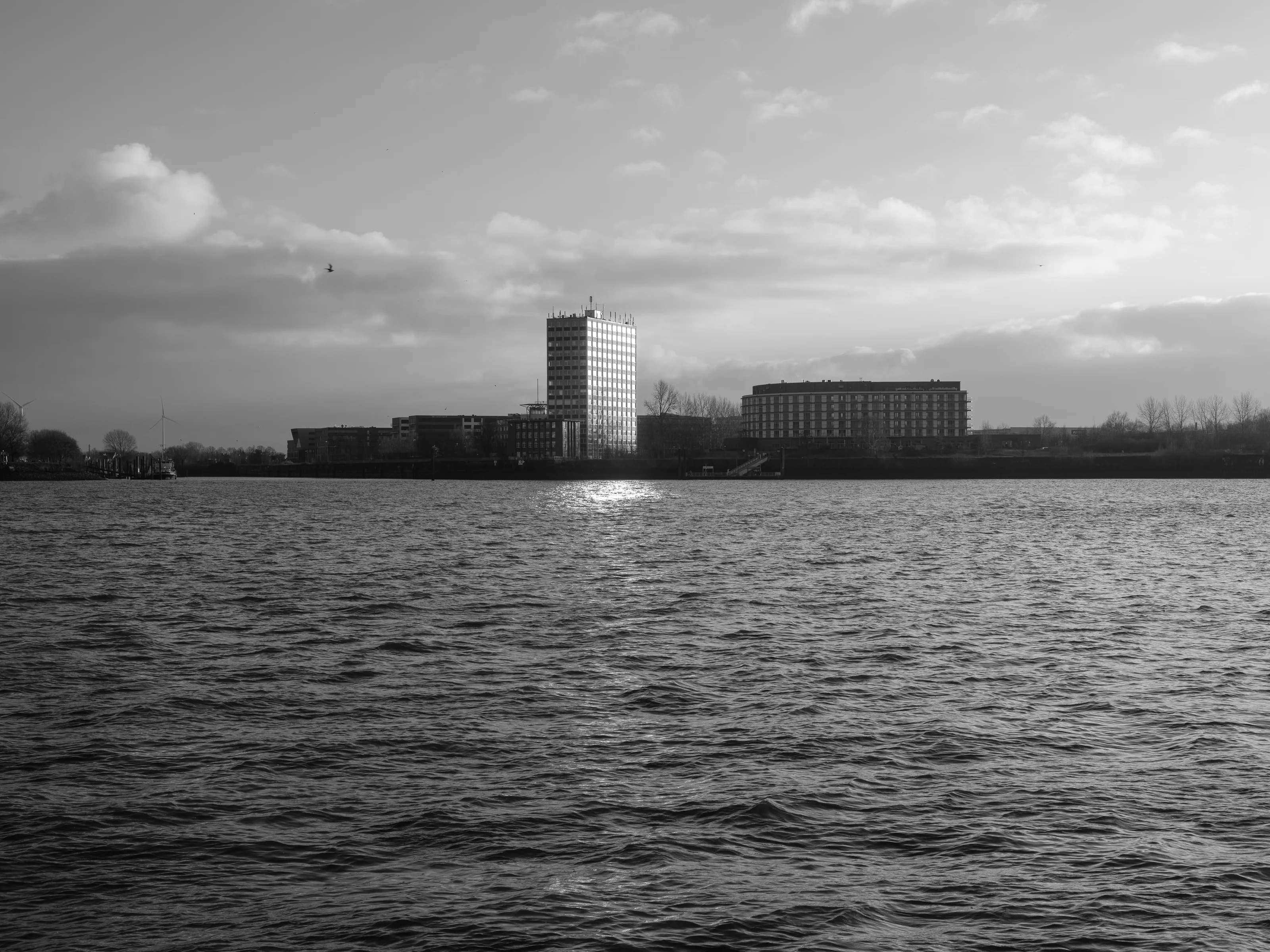 A waterfront scene with tall buildings reflecting sunlight, under a partly cloudy sky.