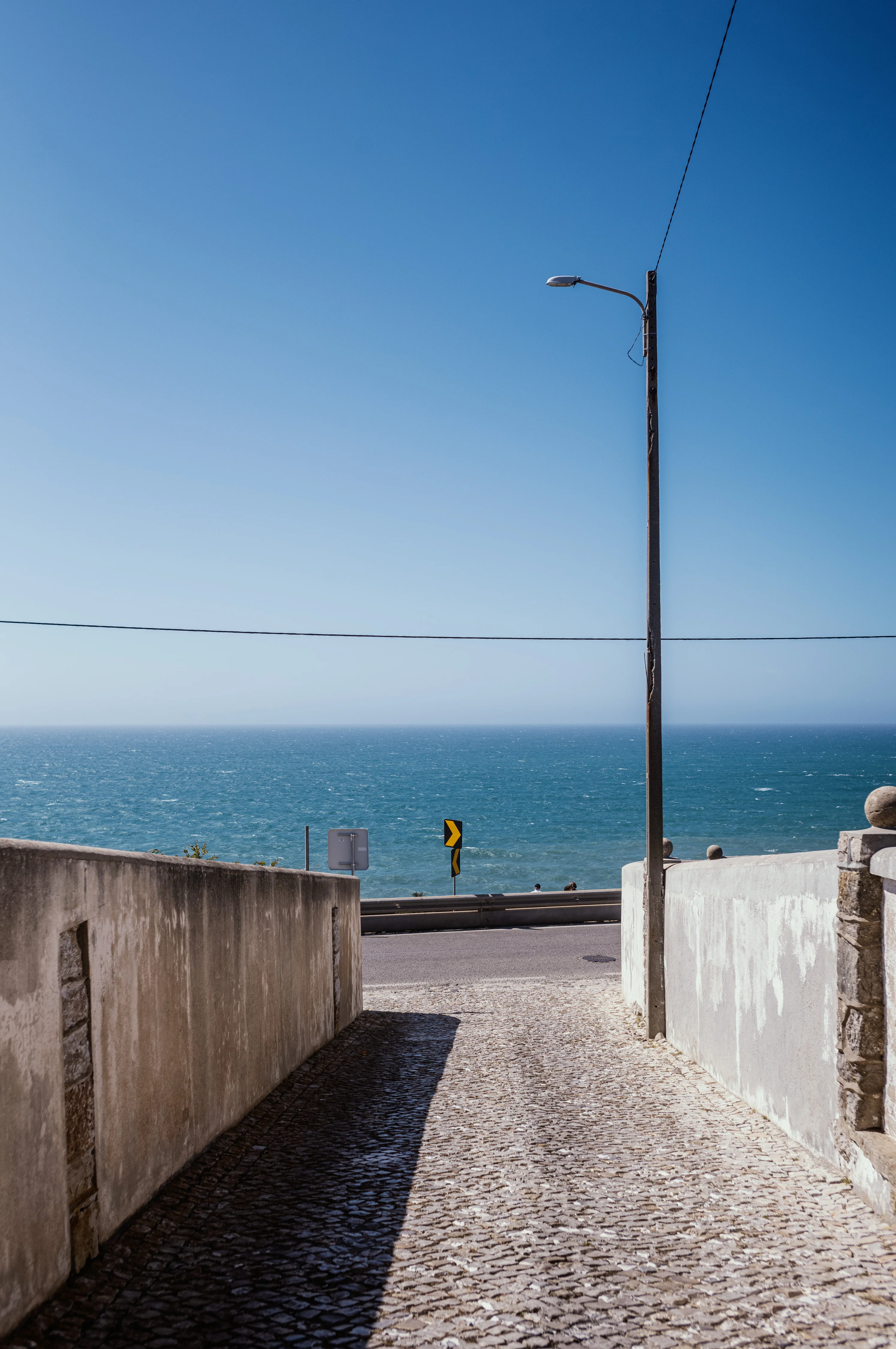 A pathway leads to a coastal road with an ocean view under a clear blue sky.