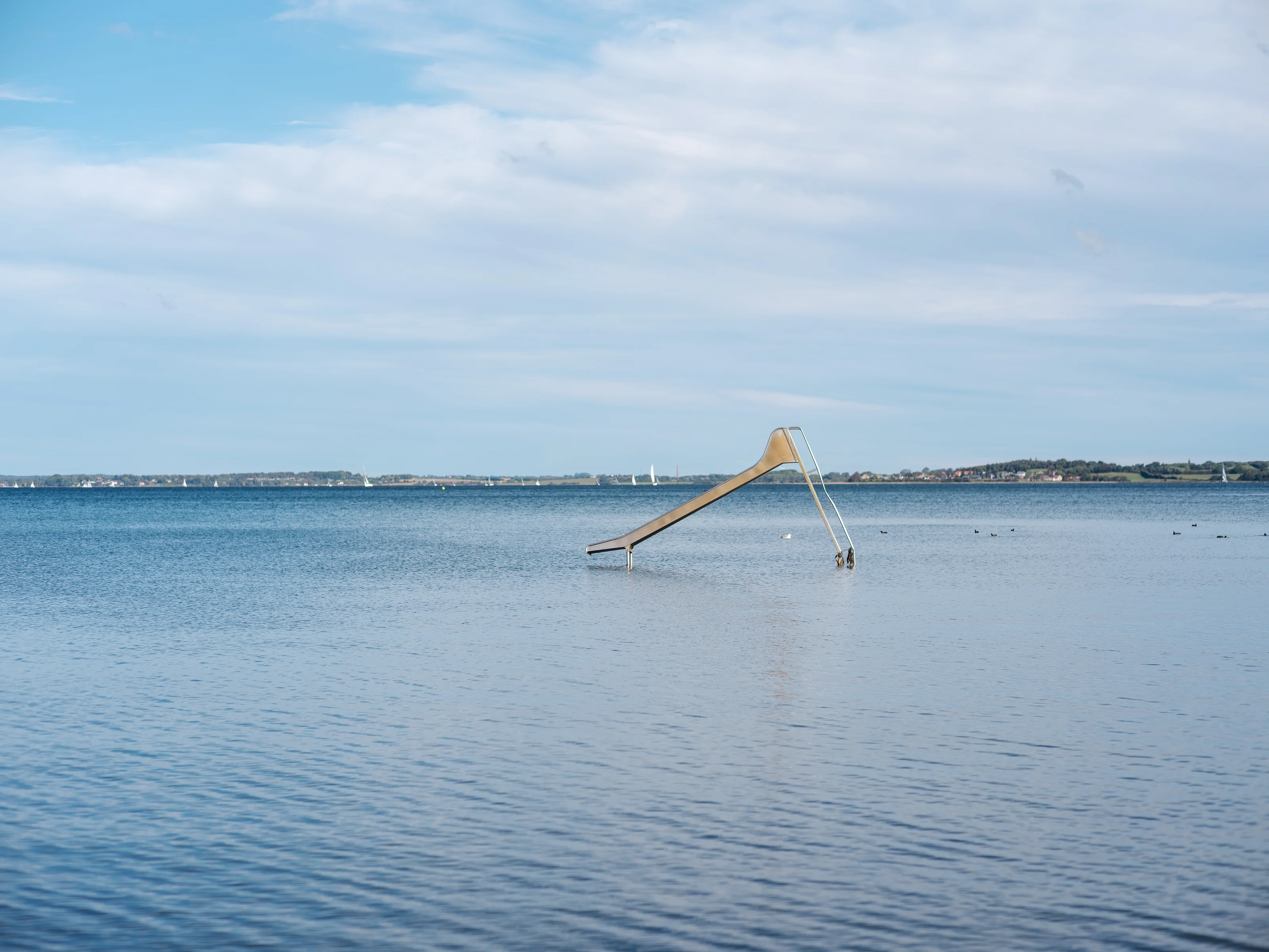 A water slide descending into a calm sea under a partly cloudy sky.