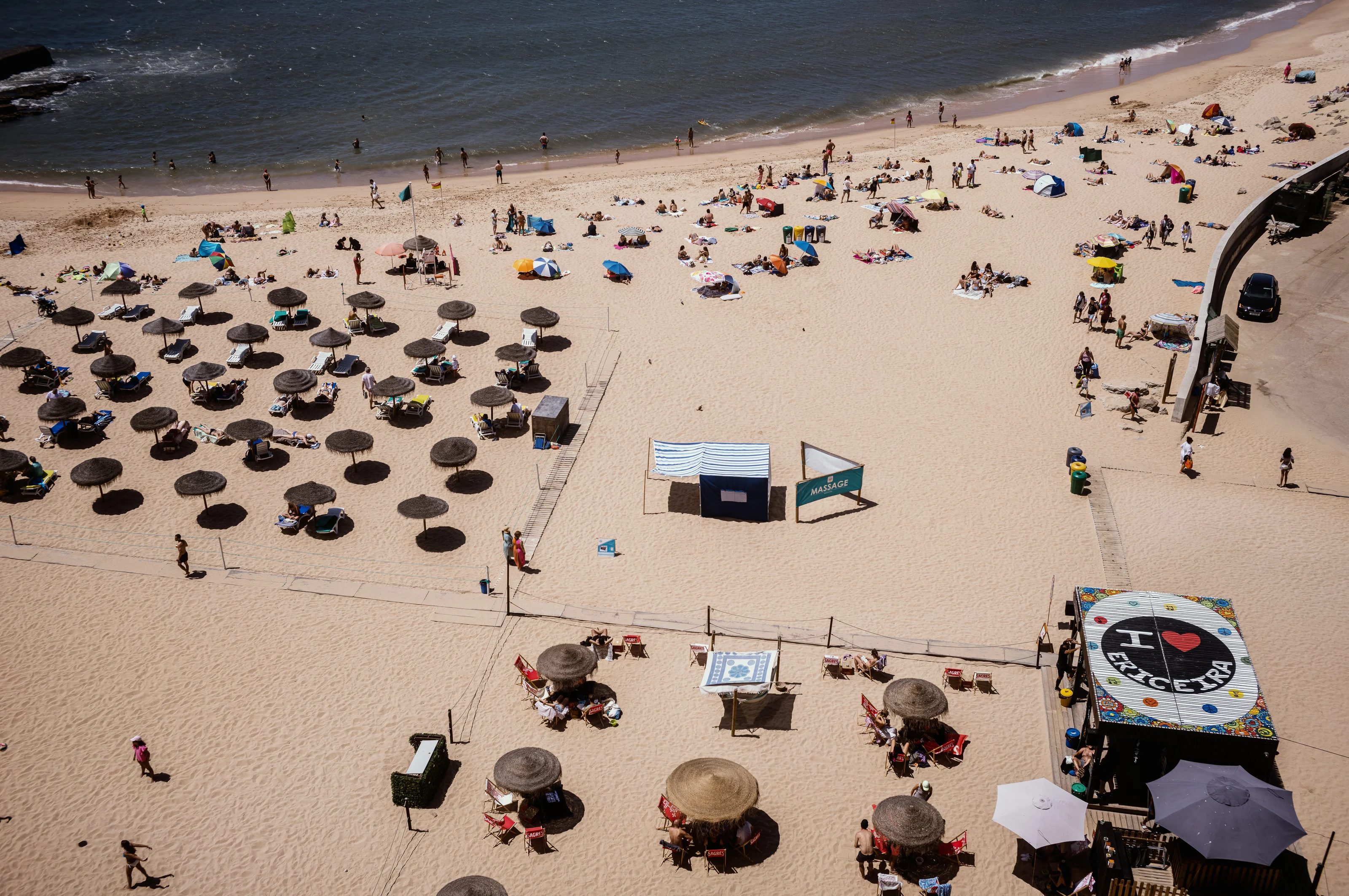 Aerial view of a sandy beach with umbrellas, sunbathers, and a massage tent.
