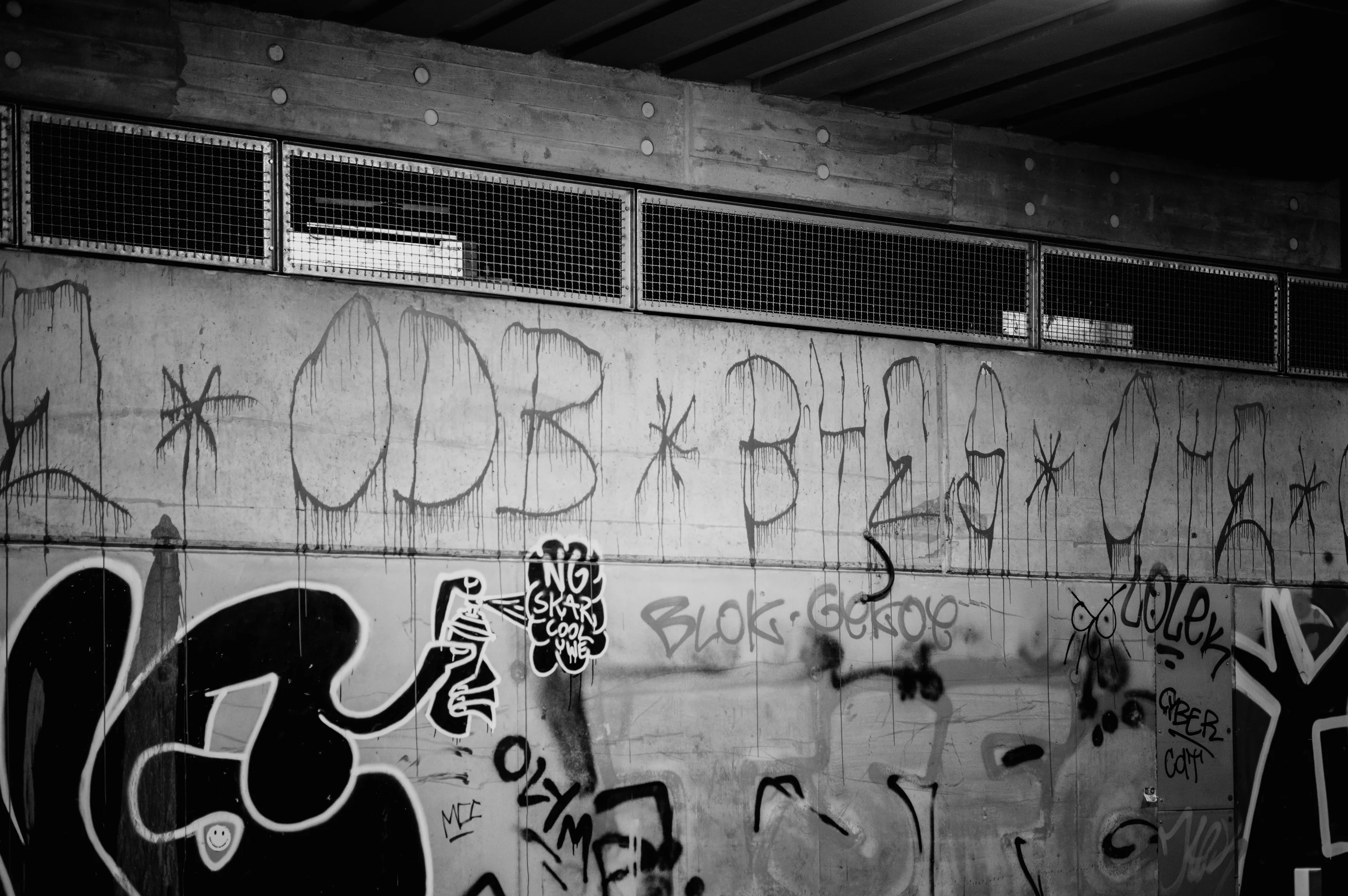 Graffiti-covered concrete wall with ventilation grates above.