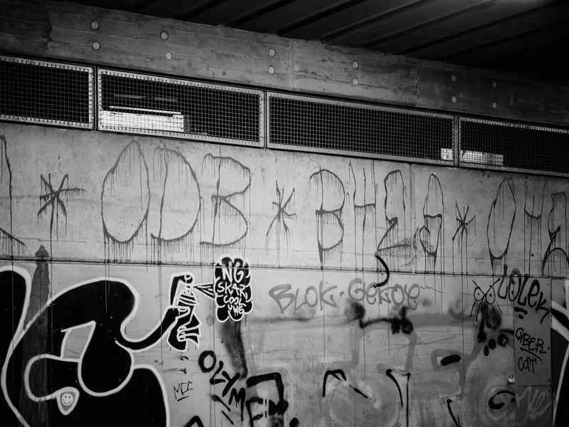 Graffiti-covered concrete wall with ventilation grates above.