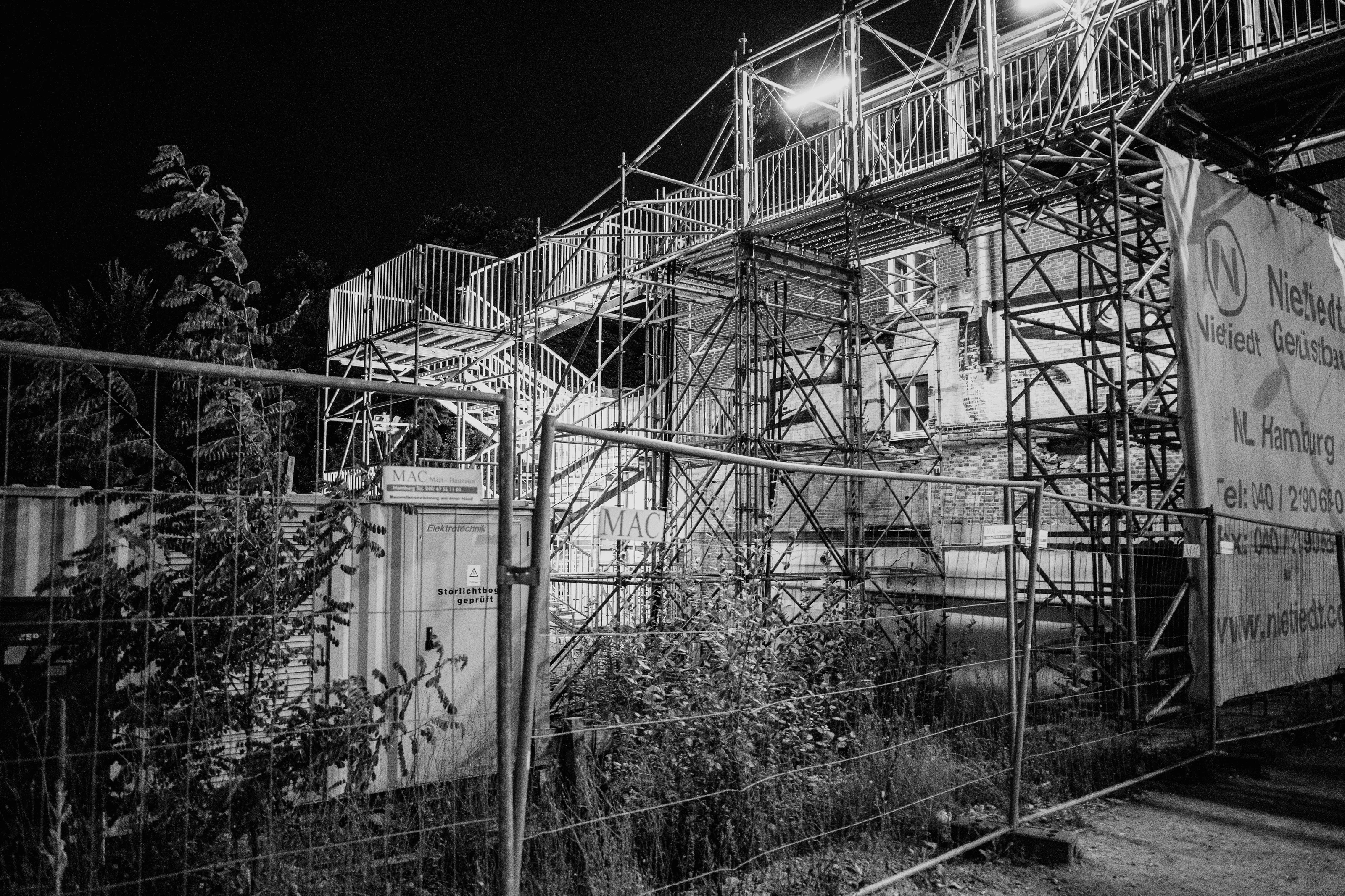 A black and white photograph of a construction site with scaffolding and lighting.
