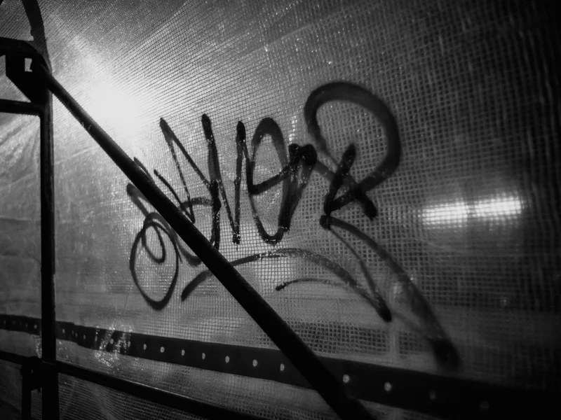 Black and white image of graffiti on a translucent surface with metal supports.