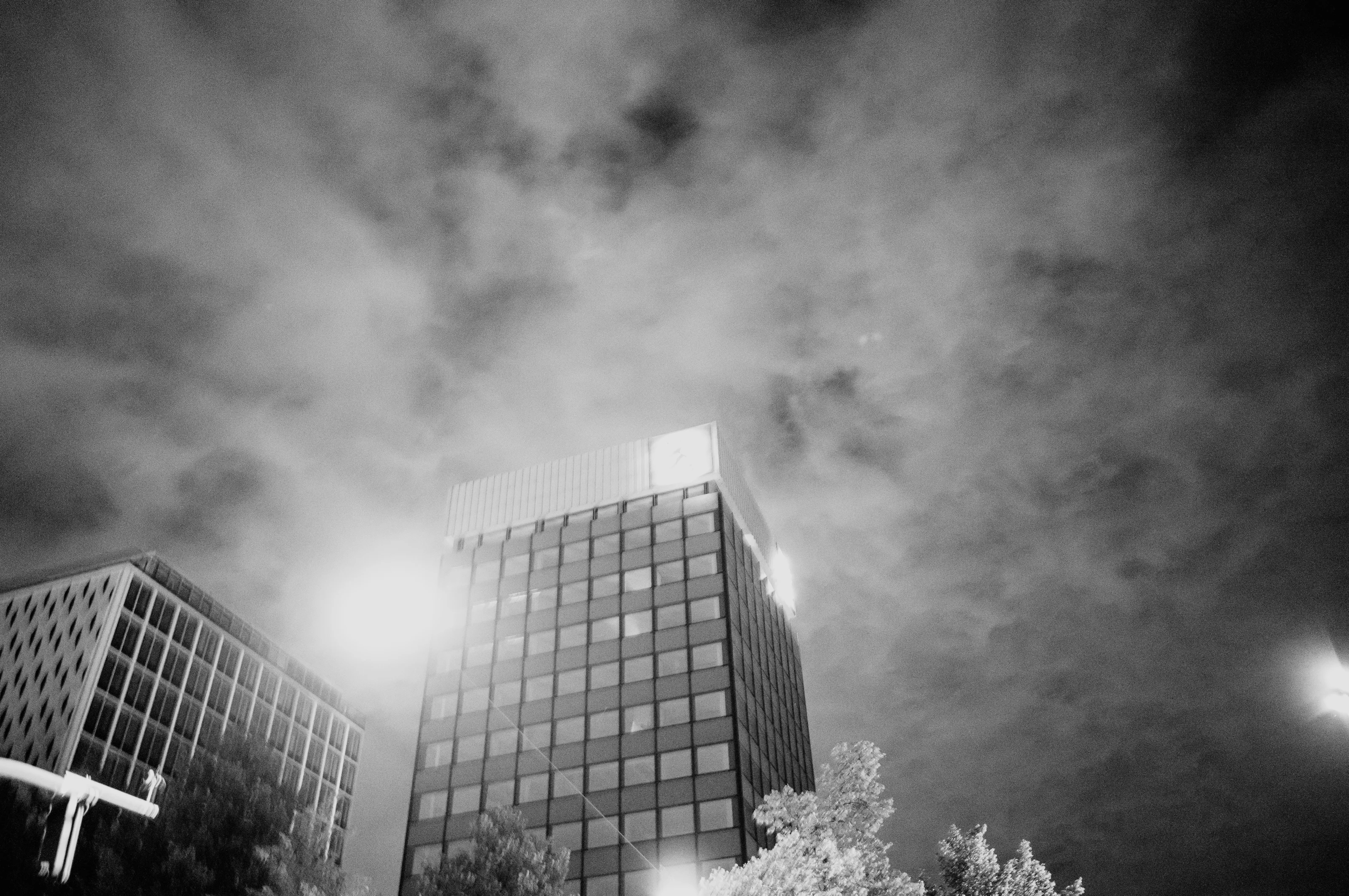 Black and white photo of tall, modern buildings with cloudy sky overhead.